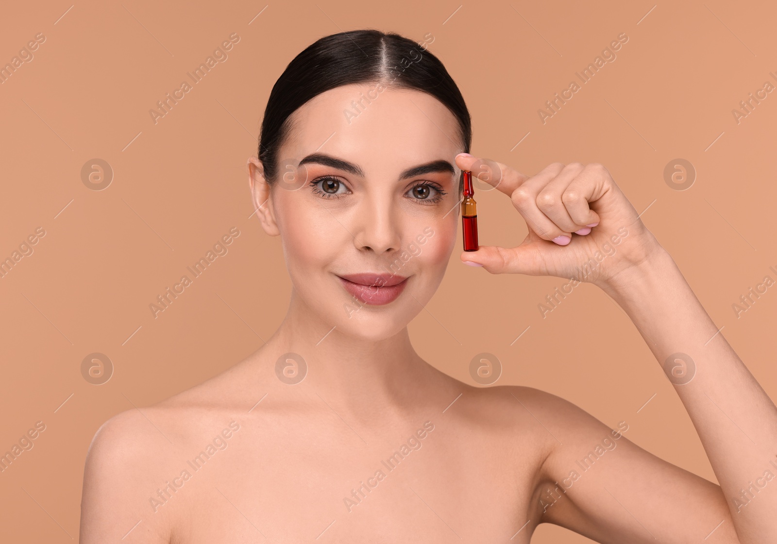 Photo of Beautiful young woman holding skincare ampoule on beige background