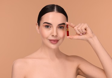 Beautiful young woman holding skincare ampoule on beige background