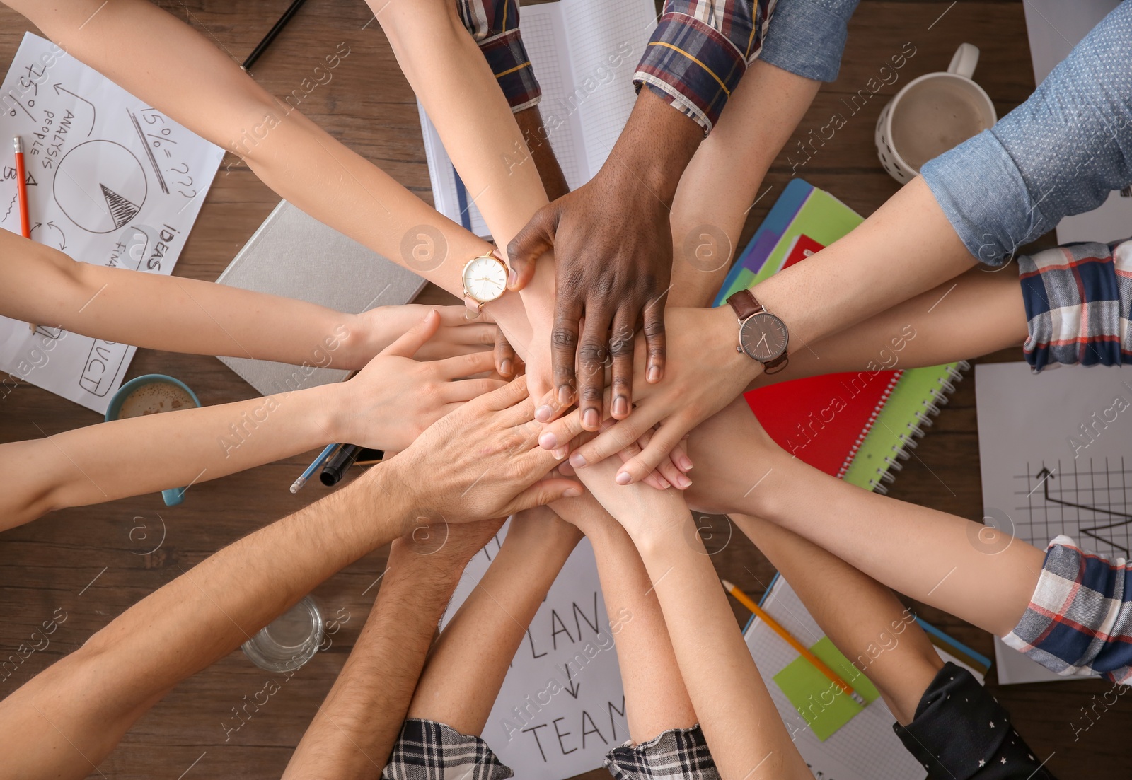 Photo of People putting hands together at table, top view. Unity concept