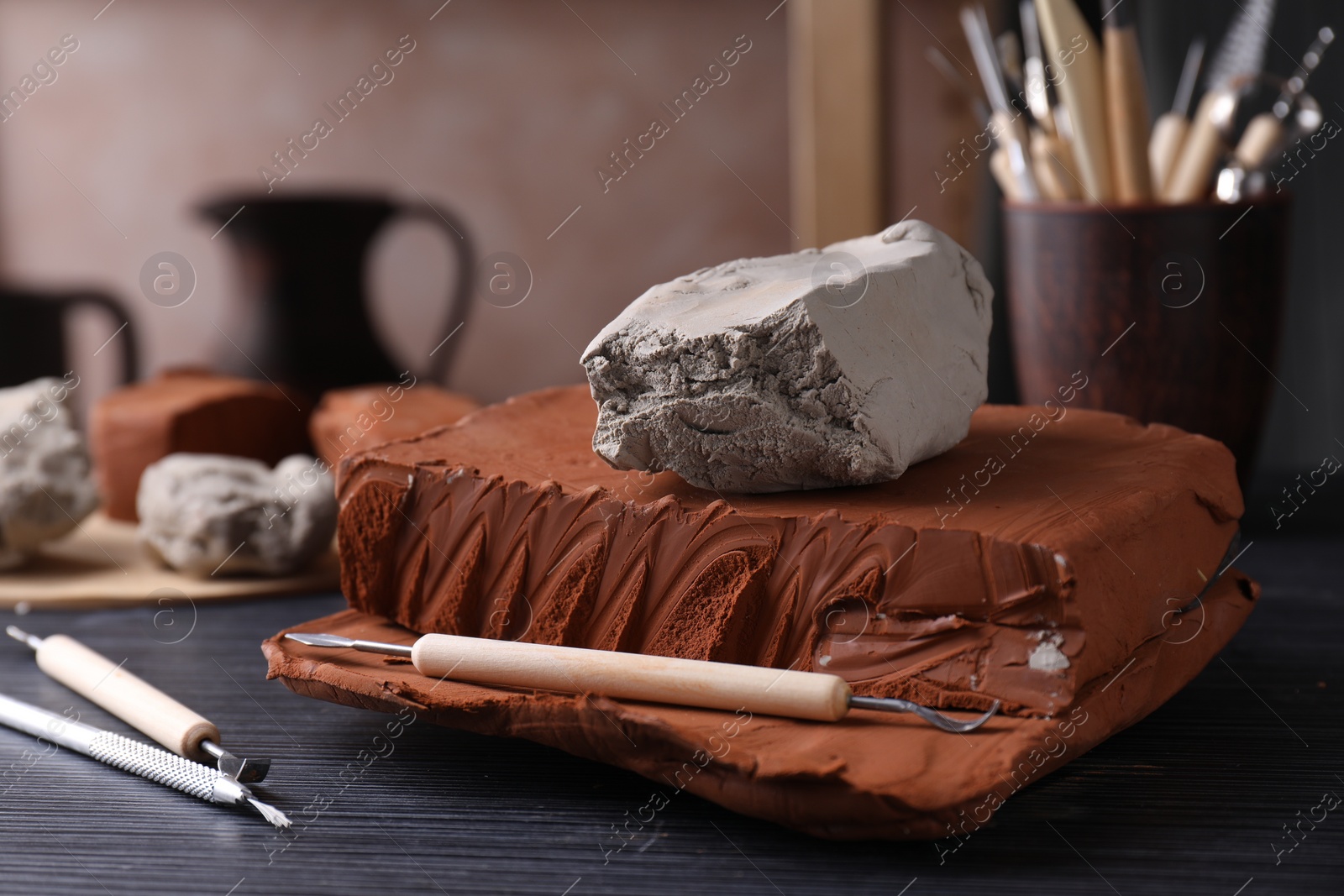 Photo of Clay and set of modeling tools on dark gray wooden table in workshop