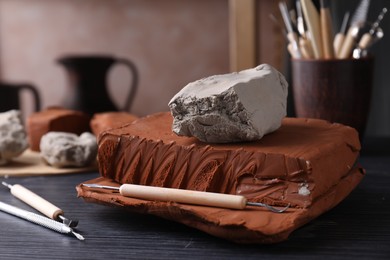 Clay and set of modeling tools on dark gray wooden table in workshop