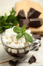 Photo of Glass cup of delicious hot chocolate with marshmallows and fresh mint on white wooden table
