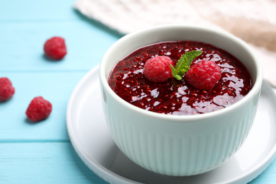 Photo of Delicious jam and fresh raspberries on light blue wooden table, closeup