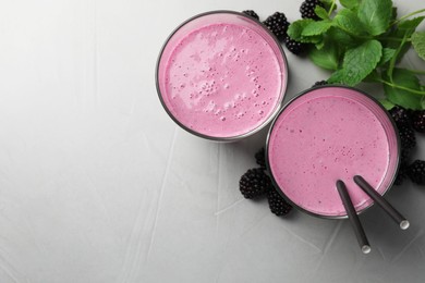 Photo of Delicious blackberry smoothie in glasses, fresh berries and mint on grey table, flat lay. Space for text