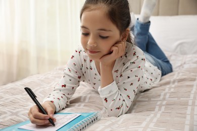 Photo of Little girl solving sudoku puzzle on bed at home