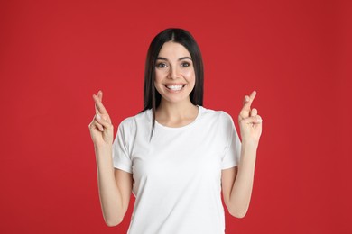 Photo of Woman with crossed fingers on red background. Superstition concept