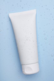 Wet tube of face cleansing product on light blue background, top view