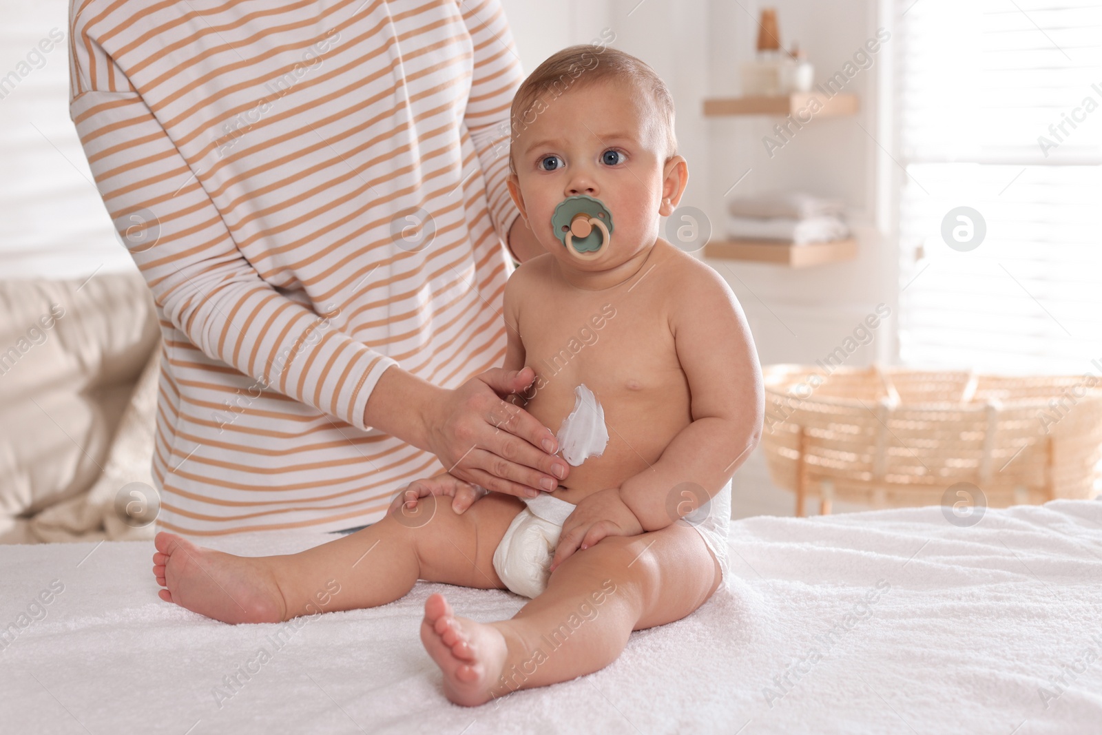 Photo of Mother applying body cream on her little baby at home, closeup