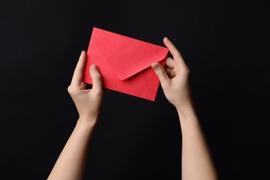 Woman holding red paper envelope on black background, closeup