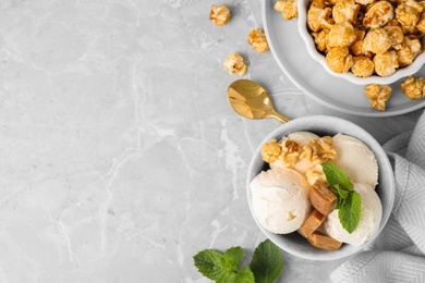 Bowl of delicious ice cream with caramel candies, popcorn and mint on light grey marble table, flat lay. Space for text