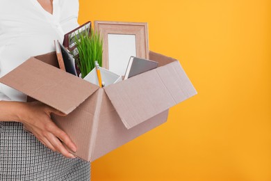 Photo of Unemployed woman with box of personal office belongings on orange background, closeup. Space for text