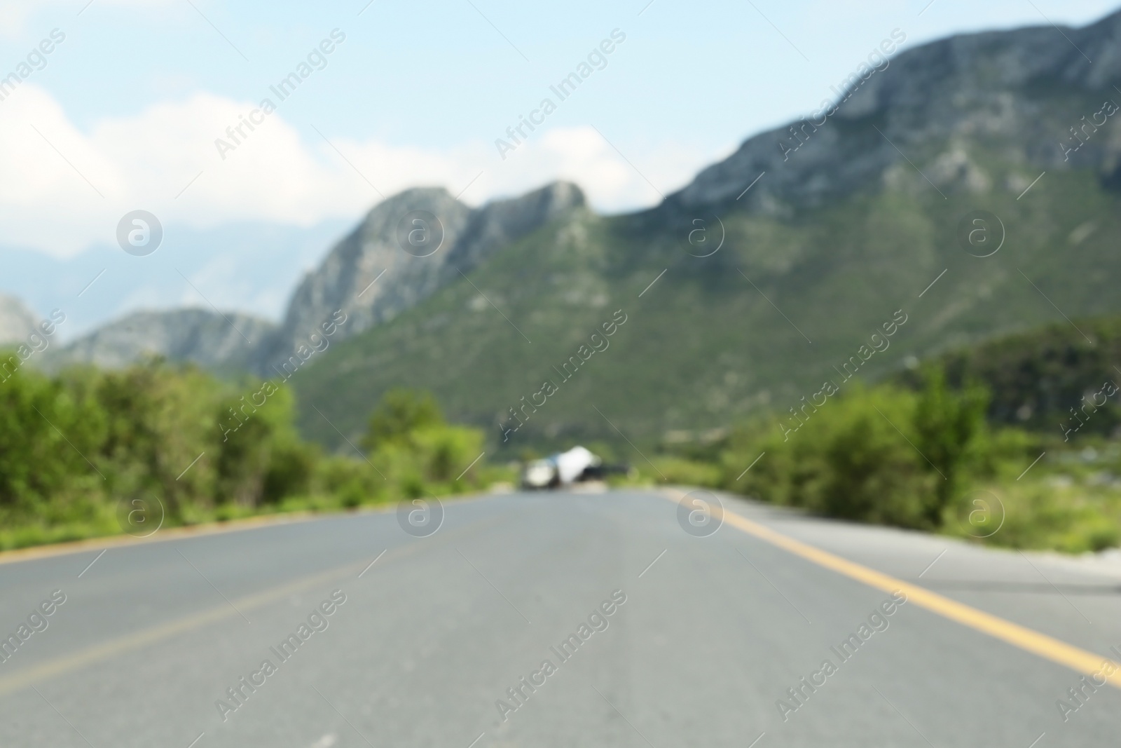 Photo of Big mountains and bushes near road under cloudy sky, blurred view