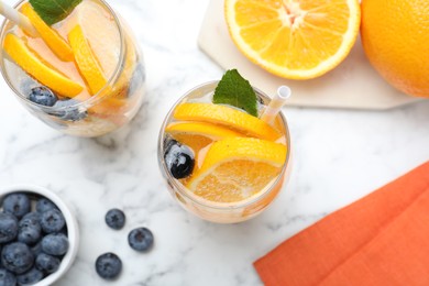 Photo of Flat lay composition of delicious orange lemonade with soda water, mint and blueberries on white marble table. Fresh summer cocktail