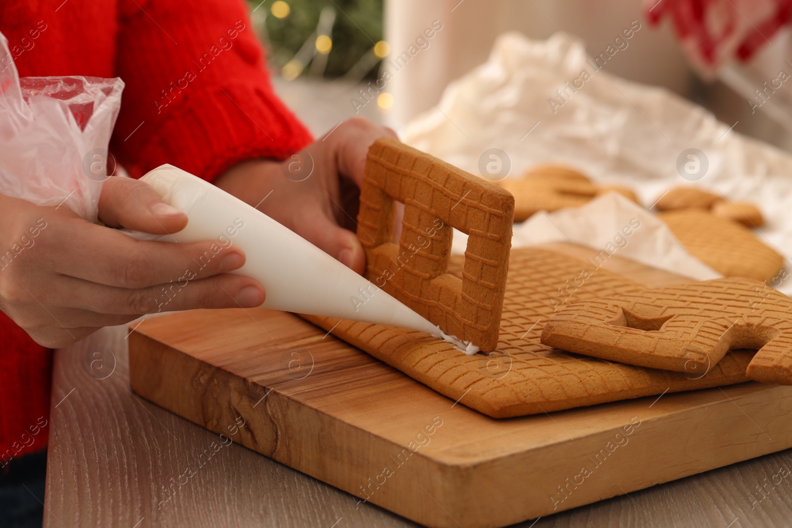 Photo of Woman making gingerbread house at wooden table, closeup