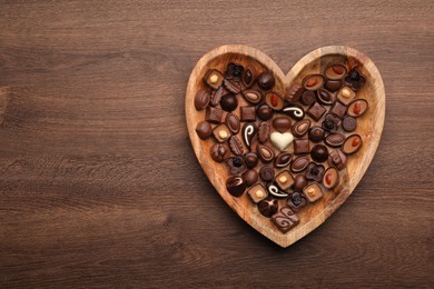 Photo of Heart shaped plate with delicious chocolate candies on wooden table, top view. Space for text