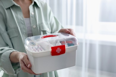 Woman holding first aid kit indoors, closeup. Space for text