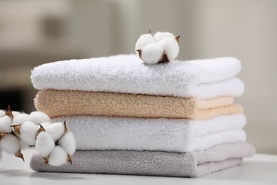 Photo of Terry towels and cotton branch with fluffy flowers on white table against blurred background, closeup