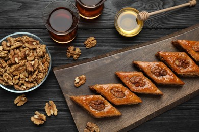 Delicious sweet baklava with walnuts, honey and hot tea on black wooden table, flat lay