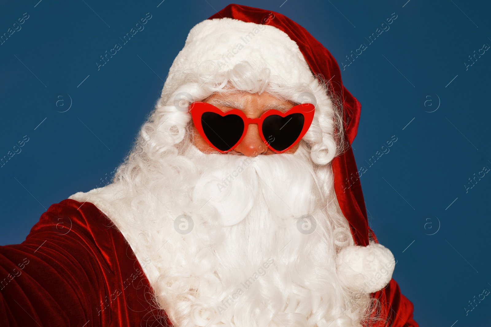 Photo of Authentic Santa Claus in sunglasses taking selfie on blue background