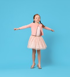 Photo of Cute little girl dancing on light blue background