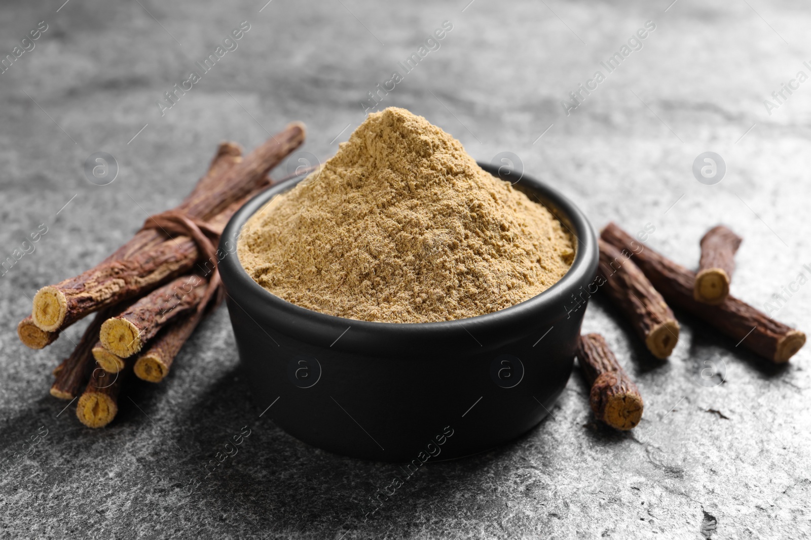 Photo of Powder in bowl and dried sticks of liquorice root on grey table