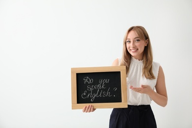 Photo of Young female teacher holding chalkboard with words DO YOU SPEAK ENGLISH? on light background. Space for text