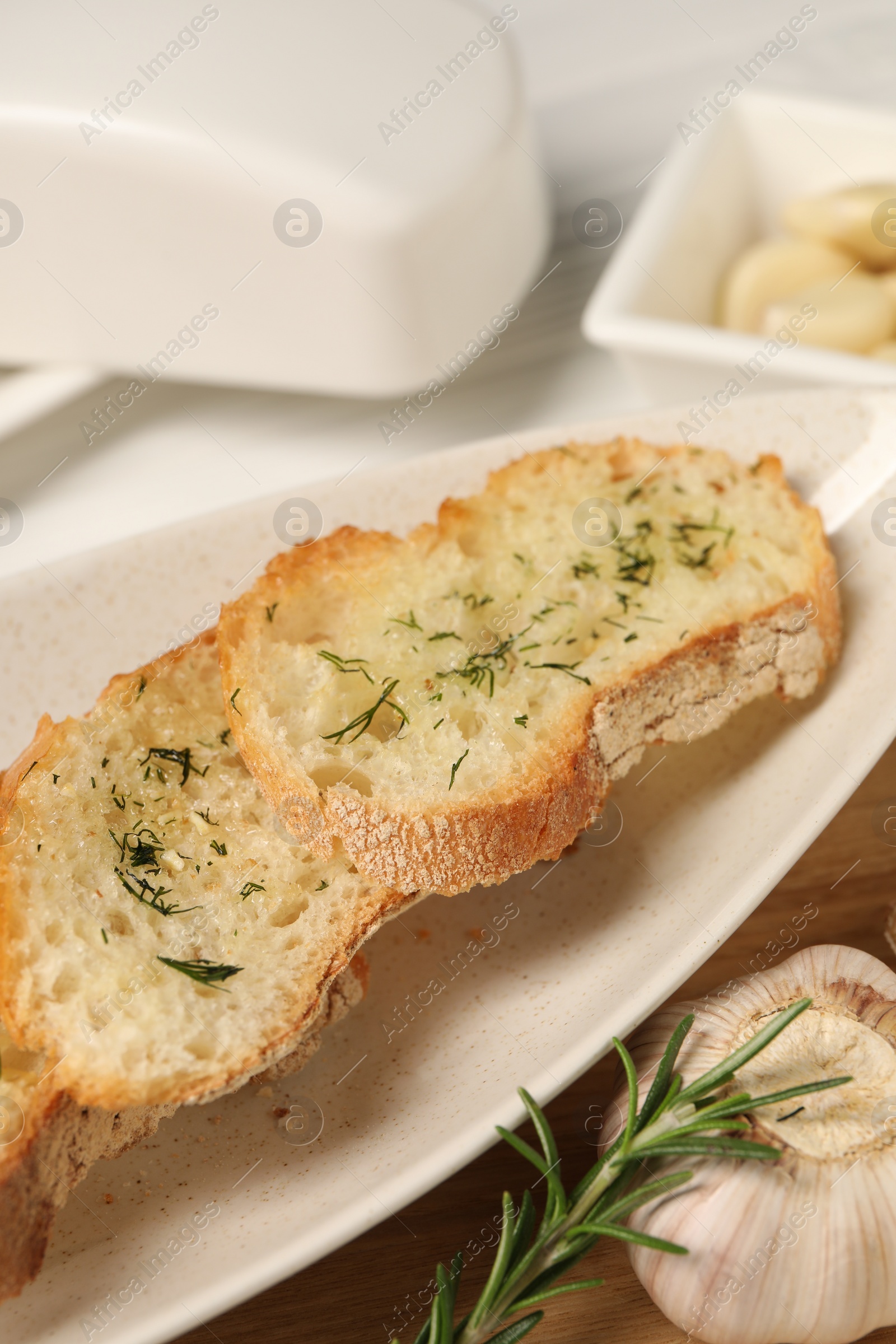 Tasty baguette with garlic, rosemary and dill on table, closeup Photo of Tasty baguette with garlic, rosemary and dill on table, closeup