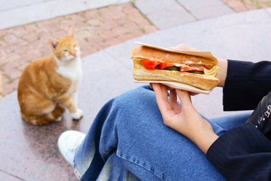 Photo of Woman holding tasty sandwich with vegetables outdoors, closeup. Street food