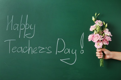 Woman holding flowers near green chalkboard with inscription HAPPY TEACHER'S DAY, closeup view