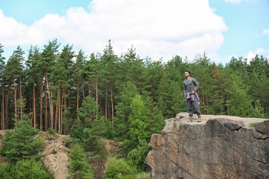 Young man on rock near beautiful forest. Camping season