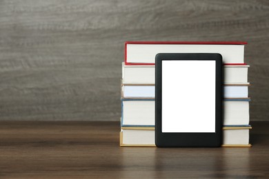 Portable e-book reader and stack of hardcover books on wooden table, space for text