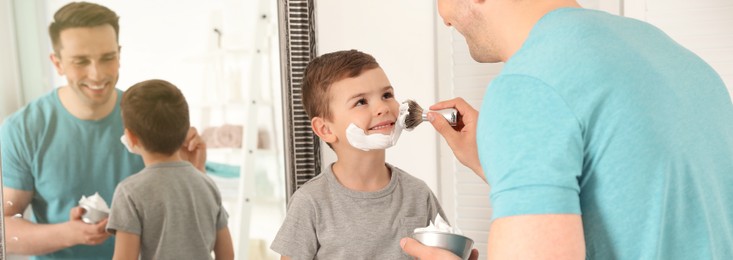 Image of Dad applying shaving foam onto son's face in bathroom. Banner design