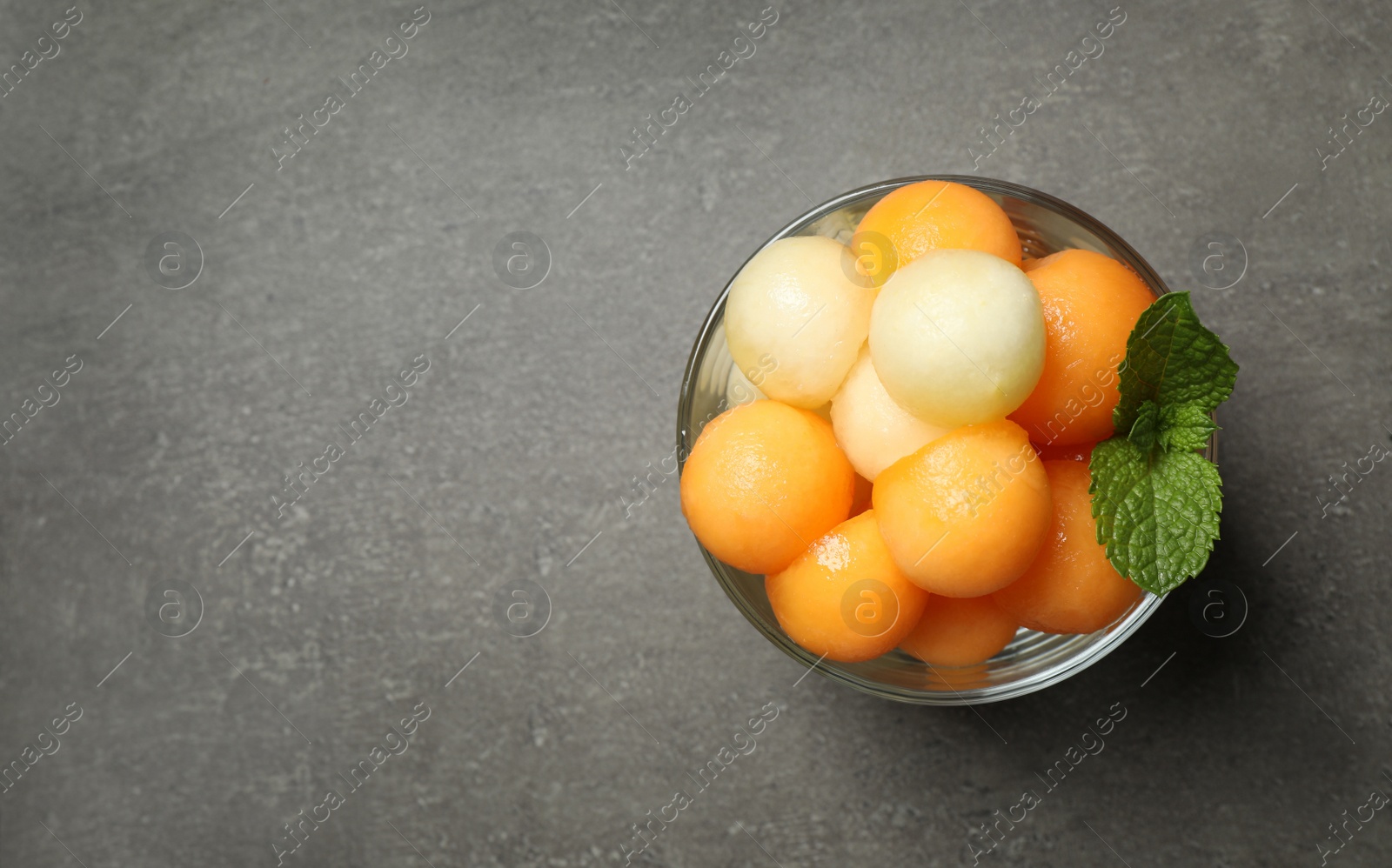 Photo of Melon balls and mint in glass on grey table, top view. Space for text