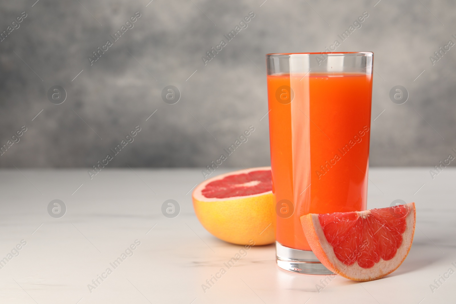 Photo of Tasty grapefruit juice in glass and fresh fruit on white table. Space for text