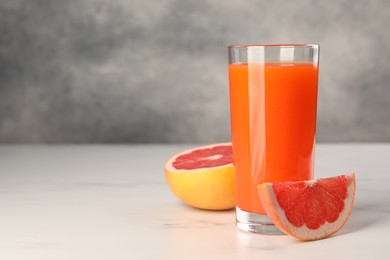 Photo of Tasty grapefruit juice in glass and fresh fruit on white table. Space for text