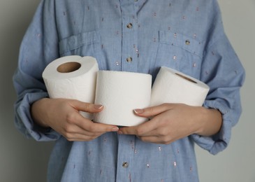 Photo of Woman with heap of toilet paper rolls on grey background, closeup