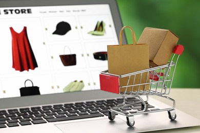 Photo of Mini cart with shopping bag and box on laptop, closeup. Online store