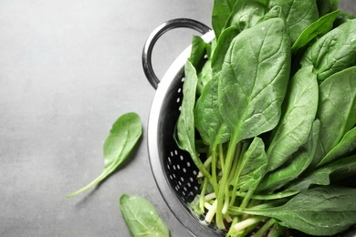 Photo of Colander with fresh green healthy spinach on grey table, top view. Space for text