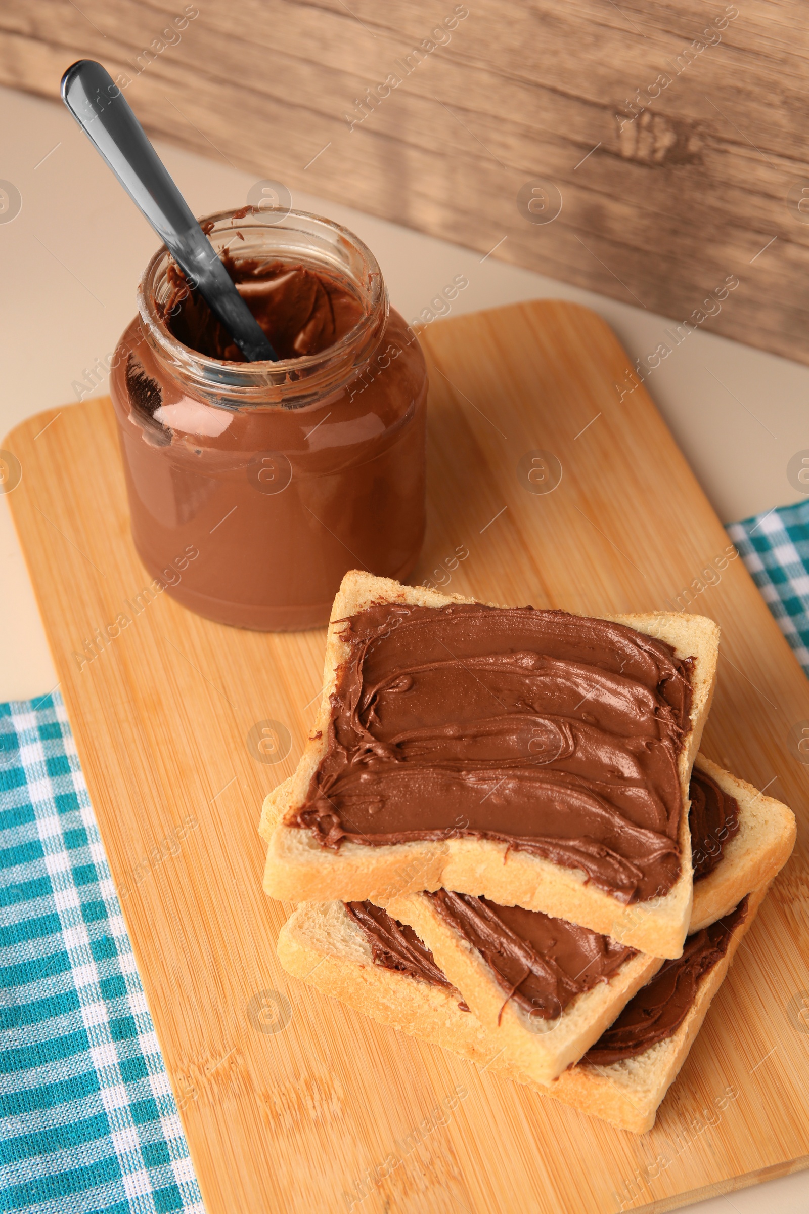 Photo of Tasty toasts with chocolate paste and jar of cream on beige table