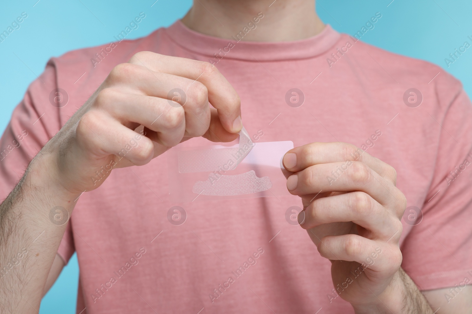 Photo of Young man with whitening strips on light blue background, closeup