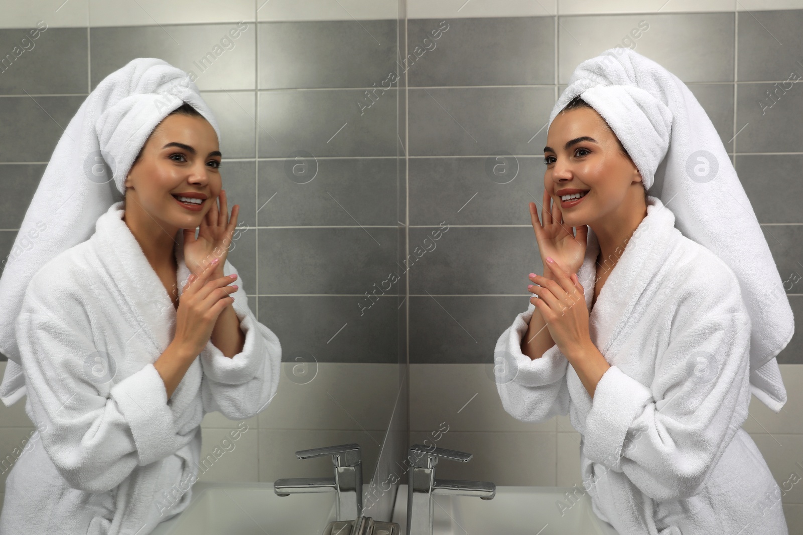 Photo of Beautiful young woman in bathrobe with towel on head near mirror at home