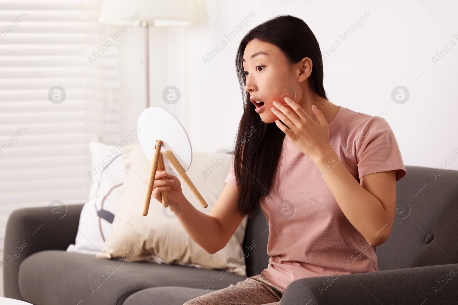 Photo of Suffering from allergy. Young woman with mirror checking her face in living room