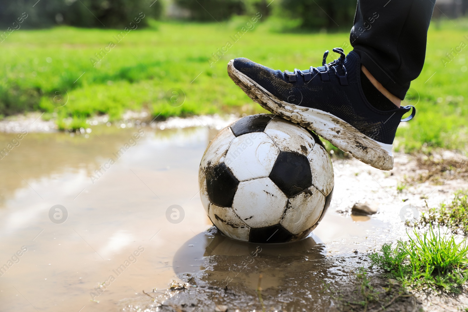 Photo of Man with dirty soccer ball near puddle outdoors, closeup