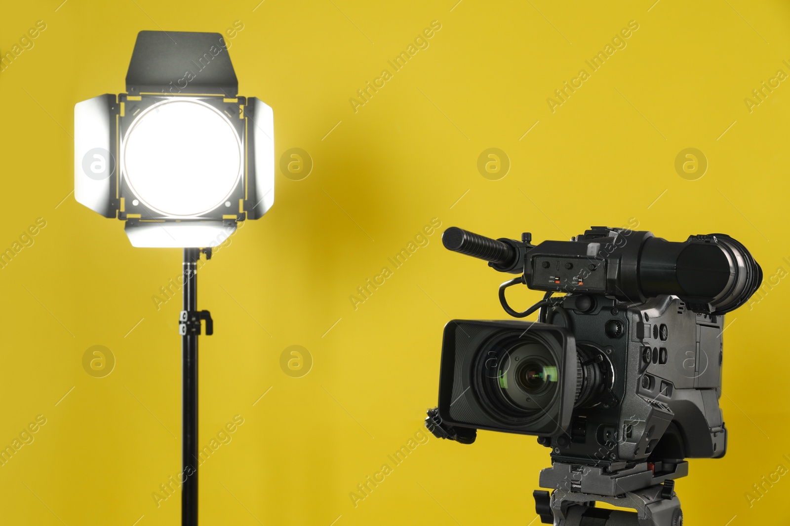 Photo of Professional video camera and lighting equipment on yellow background