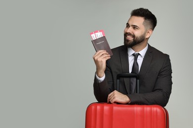 Photo of Happy businessman with passport, tickets and suitcase on grey background. Space for text