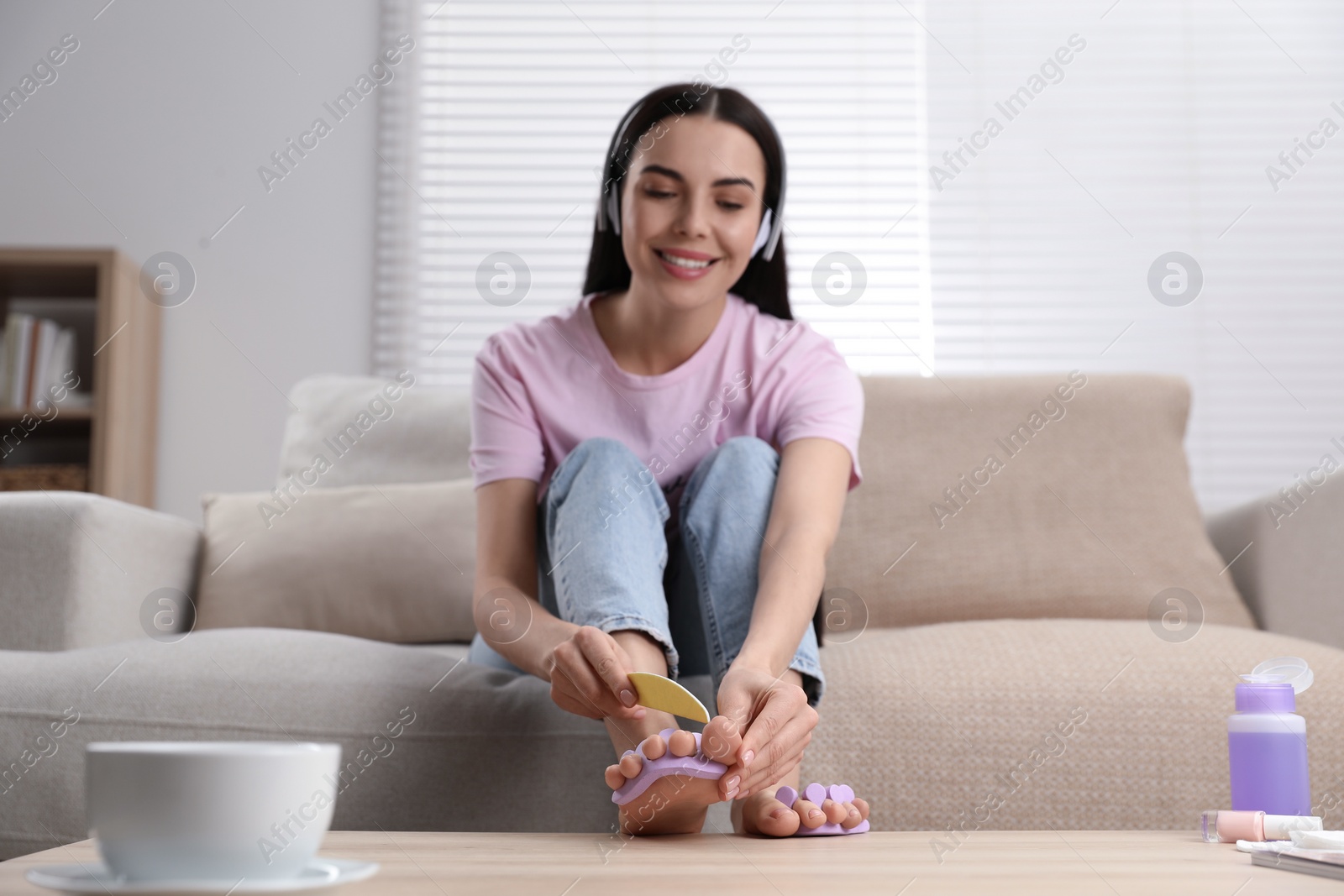 Photo of Beautiful young woman listening to music while giving herself pedicure in living room, selective focus