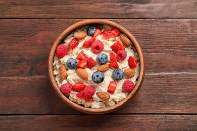 Photo of Tasty oatmeal porridge with berries and almond nuts in bowl on wooden table, top view