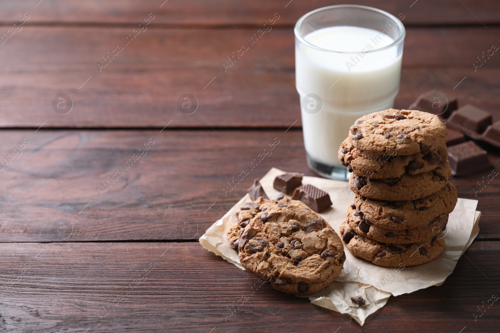 Photo of Delicious chocolate chip cookies and glass of milk on wooden table, space for text