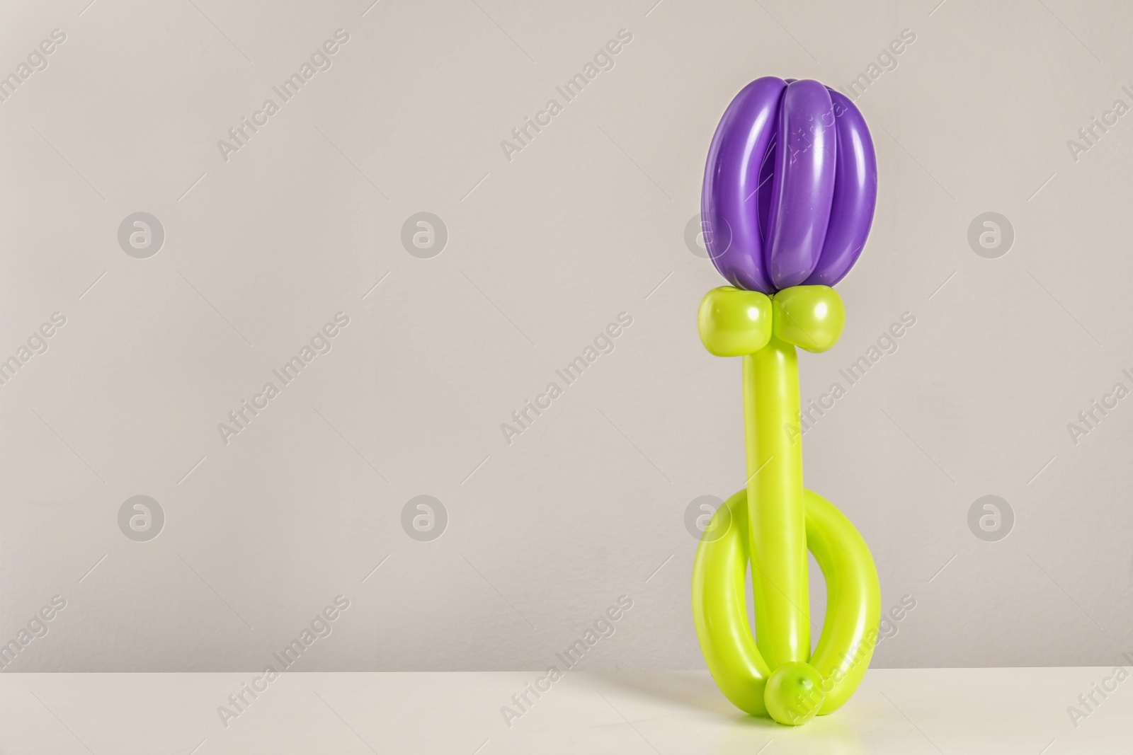 Photo of Flower figure made of modelling balloon on table against color background. Space for text