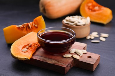 Photo of Glass bowl of pumpkin seed oil on dark grey table